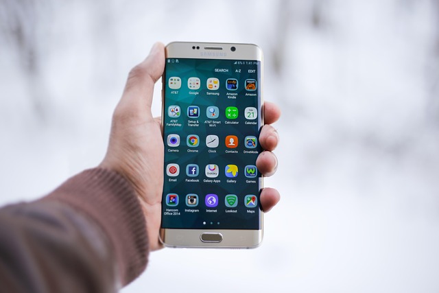 A hand holding a smartphone showing mobile app icons