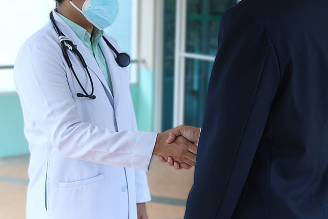 A doctor in a lab coat and mask shaking hands with a patient