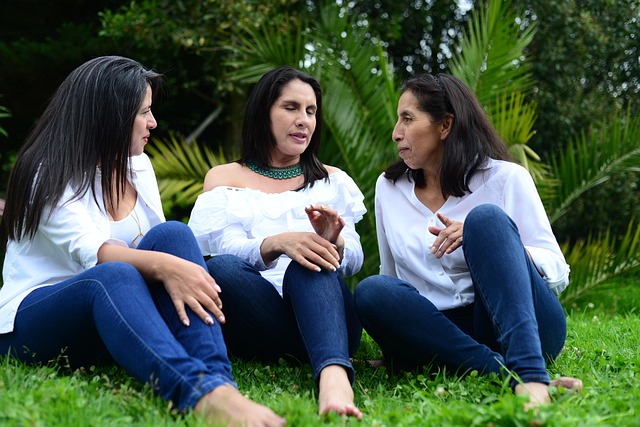 Three women sitting on grass talking to each other
