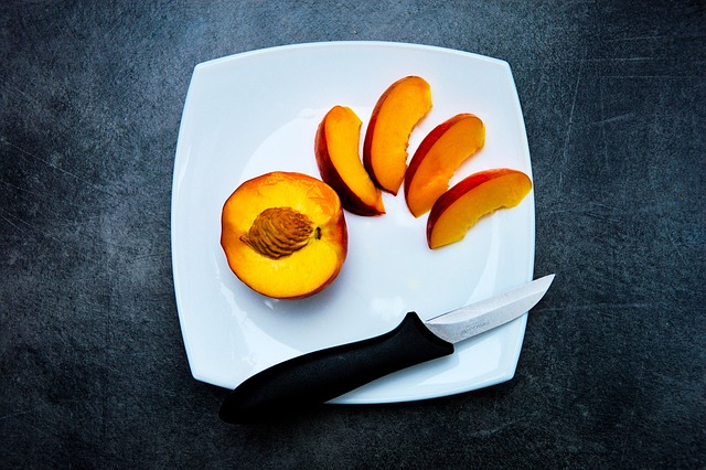 Sliced fresh peach and knife on a white square plate