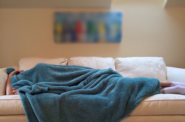 A person resting on a couch covered in a blanket