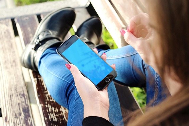 A person holding a smartphone while sitting on a wooden bench