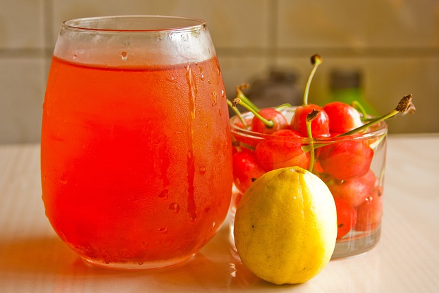 A glass of red drink next to a lemon and cherries