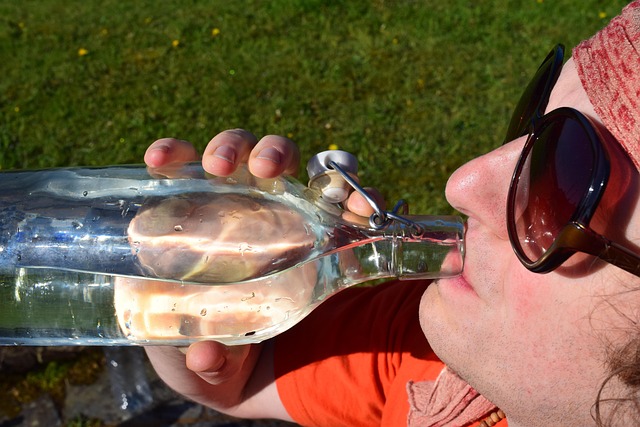 A person drinking water directly from a glass bottle